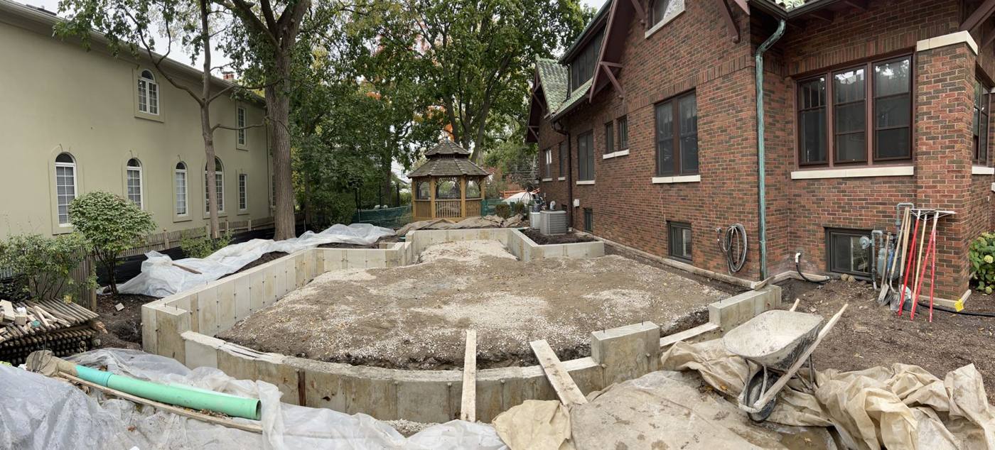 Stripped foundation walls with angled corners between a brick bungalow, the neighbor's house and a backyard gazebo