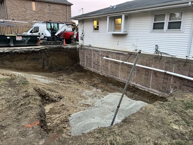 Excavation dug down along the back foundation wall of a white ranch house