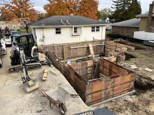 Wall forms set around the addition with a mini excavator beside them
